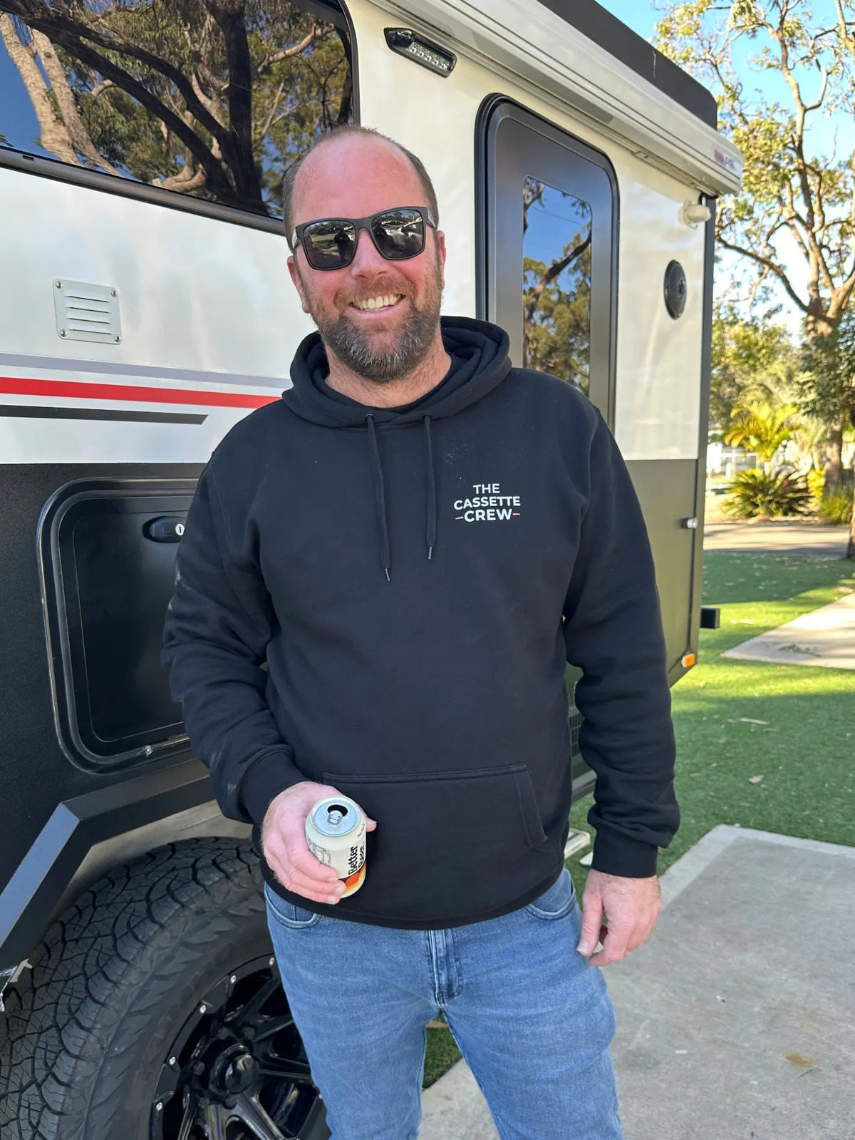 A Cassette Crew member with a drink beside a caravan at happy hour